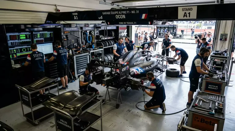 Garage d'écurie F1 avec monoplaces et mécaniciens préparant une voiture de course